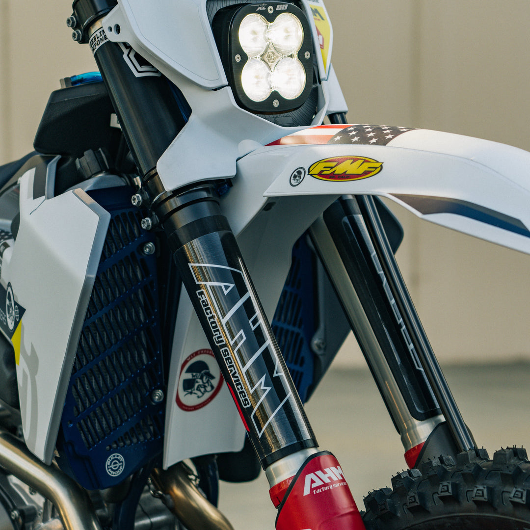 Close-up image of a motorcycle's front fork with upper fork guards installed, featuring a gloss black finish.